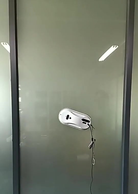 Robot limpiavidrios adherido a una puerta de vidrio con su cuerda de seguridad